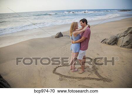 Young couple standing in heart design on beach View Large Photo Image Stock Image - Young couple standing in heart design on beach. Fotosearch