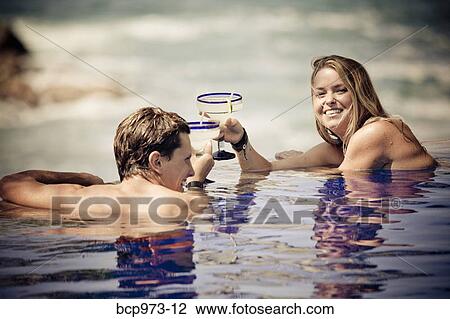 Stock Image - Young couple with cocktails in infinity pool. Fotosearch