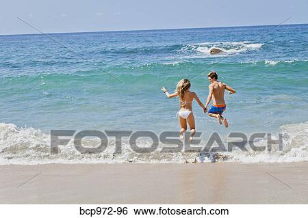 Stock Photograph - Young man and woman jumping in surf. Fotosearch