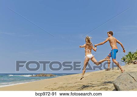 Stock Image - Young man and woman running on beach. Fotosearch