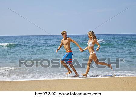 Stock Image - Young man and woman running on beach. Fotosearch