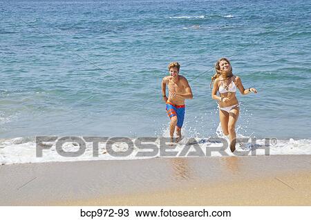 Stock Image - Young man and woman running on beach. Fotosearch