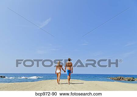 Stock Image - Young man and woman walking toward shore. Fotosearch
