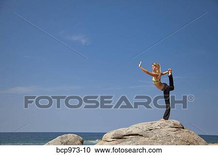 Young woman in yoga pose on rock by ocean View Large Photo Image Stock Image - Young woman in yoga pose on rock by ocean. Fotosearch