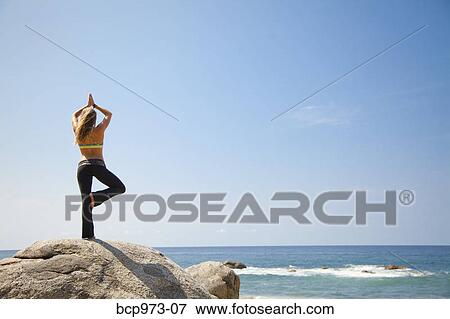 Young woman in yoga pose on rock by ocean View Large Photo Image Stock Photo - Young woman in yoga pose on rock by ocean. Fotosearch