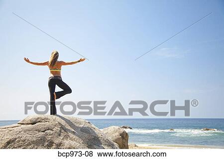 Young woman in yoga pose on rock by ocean View Large Photo Image Stock Photo - Young woman in yoga pose on rock by ocean. Fotosearch