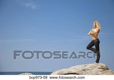Young woman in yoga pose on rock by ocean View Large Photo Image Stock Photo - Young woman in yoga pose on rock by ocean. Fotosearch