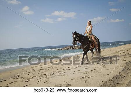Stock Image - Young woman riding horse on beach. Fotosearch