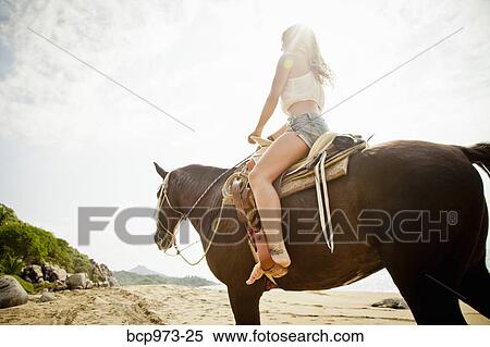 Stock Photography - Young woman riding horse on beach. Fotosearch