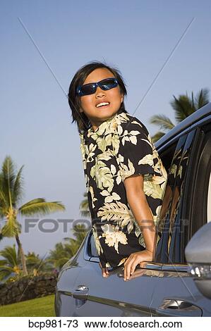 Boy in Hawaiian shirt leans out a car window against a tropical background View Large Photo Image Stock Image - Boy in Hawaiian shirt leans out a car window against a tropical background. Fotosearch