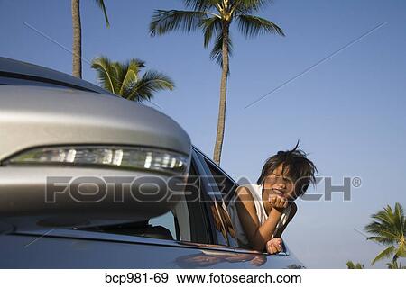 Stock Photo - Boy leans out a car window against a tropical background. Fotosearch