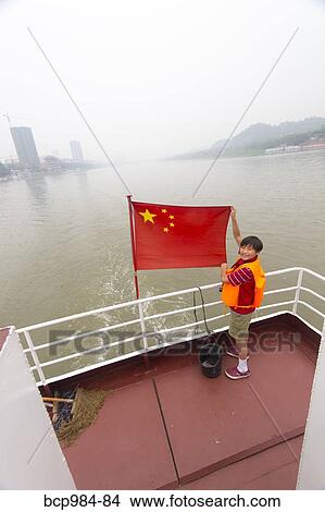Picture - "Boy on a tour boat holding a Chinese flag, Leshan, Sichuan province, China". Fotosearch