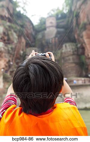 Stock Photograph - "Boy photographing the Leshan giant Buddha from a riverboat, Sichuan province, China". Fotosearch