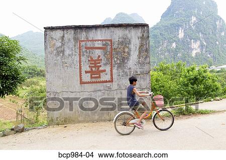 "Boy rides a bicycle past a ""one good deed"" sign in the countryside, Yangshuo, China" View Large Photo Image Picture - "Boy rides a bicycle past a ""one good deed"" sign in the countryside, Yangshuo, China". Fotosearch