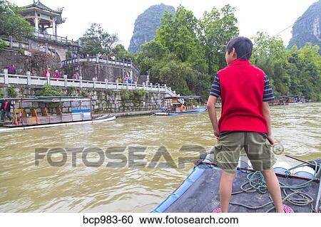 Stock Image - "Boy standing on a bamboo raft on the Li River, Yangshuo, China". Fotosearch