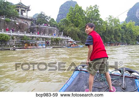 Stock Photo - "Boy standing on a bamboo raft on the Li River, Yangshuo, China". Fotosearch