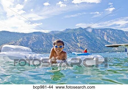 Boy swims with a toy floatie in a lake View Large Photo Image Picture - Boy swims with a toy floatie in a lake. Fotosearch