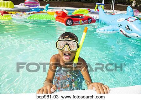 Stock Image - Boy wearing a scuba mask and snorkel swims in a pool full of inflatable toys. Fotosearch