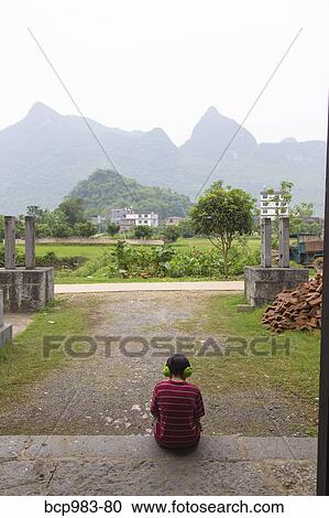 Boy wearing headphones uses an electronic device in a rural Chinese village View Large Photo Image Stock Image - Boy wearing headphones uses an electronic device in a rural Chinese village. Fotosearch