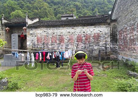 Boy wearing headphones uses an electronic device in a rural Chinese village View Large Photo Image Stock Photo - Boy wearing headphones uses an electronic device in a rural Chinese village. Fotosearch