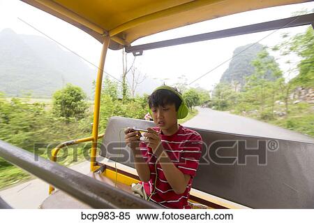 Boy wearing headphones uses an electronic device while riding a village jitney View Large Photo Image Stock Photography - Boy wearing headphones uses an electronic device while riding a village jitney. Fotosearch