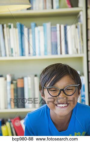Boy wearing vintage glasses smiles in front of a bookcase View Large Photo Image Stock Photo - Boy wearing vintage glasses smiles in front of a bookcase. Fotosearch