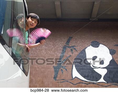 Stock Photo - Boy with a pink fan leaning out of a tour bus. Fotosearch