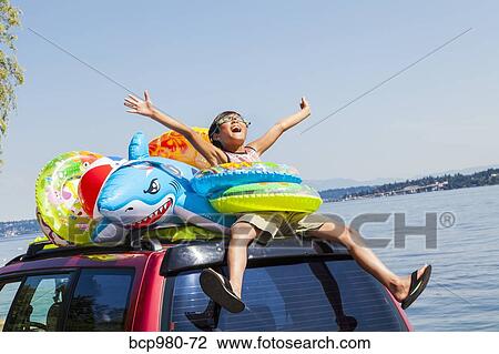 Child poses beach toys and floaties on the roof of a car View Large Photo Image Stock Image - Child poses beach toys and floaties on the roof of a car. Fotosearch