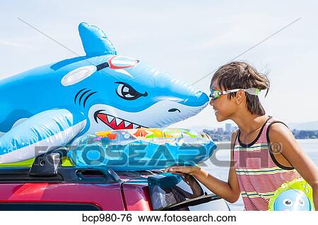 Stock Photograph - Child poses beach toys and floaties on the roof of a car. Fotosearch