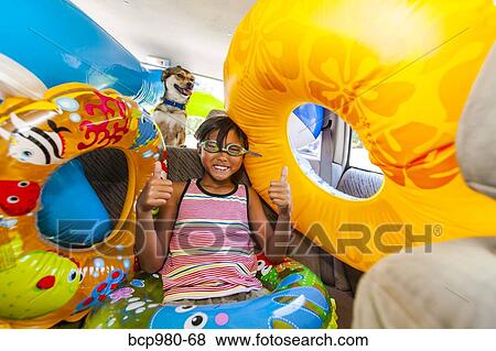 Stock Photo - Child poses with his dog in a car full of beach toys and floaties. Fotosearch