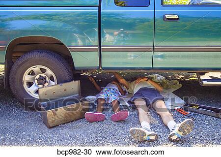 Stock Image - "Man and a boy lying under a vehicle with a toolbox, doing repairs". Fotosearch