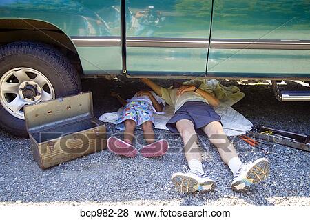 Stock Photo - "Man and a boy lying under a vehicle with a toolbox, doing repairs". Fotosearch