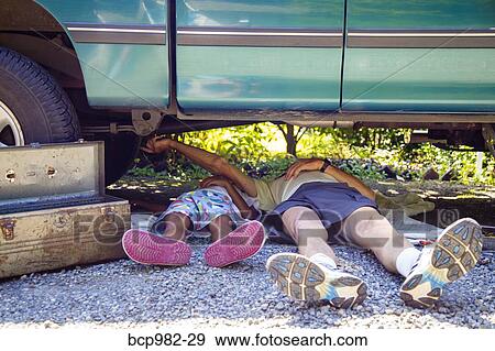 Stock Photo - "Man and a boy lying under a vehicle with a toolbox, doing repairs". Fotosearch