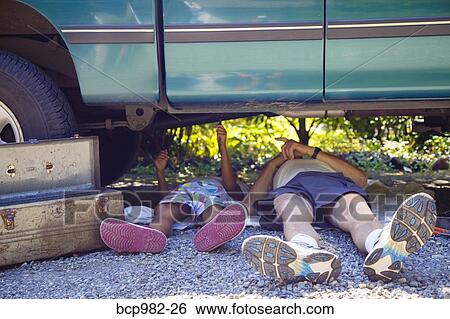 Stock Photograph - "Man and a boy lying under a vehicle with a toolbox, doing repairs". Fotosearch