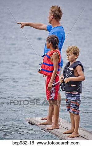 Stock Photo - Man and two boys standing on a dock in a lake. Fotosearch