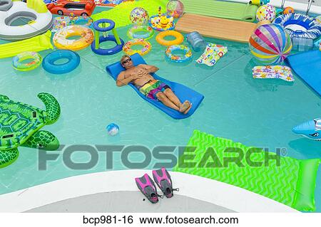 Man floats in a pool full of inflatable toys View Large Photo Image Stock Photograph - Man floats in a pool full of inflatable toys. Fotosearch