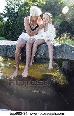 Portrait of a grandmother and granddaughter sitting on a stone bridge over a small creek View Large Photo Image Picture - Portrait of a grandmother and granddaughter sitting on a stone bridge over a small creek. Fotosearch