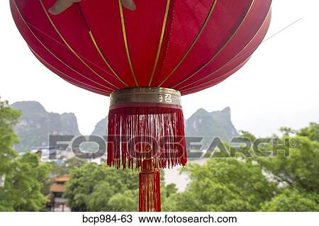 Stock Image - "Red lantern hanging in front of a view of the Karst mountains and Li River, Yangshuo, China". Fotosearch