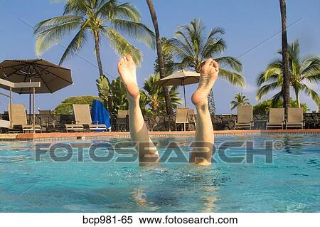 Stock Photography - View of a woman's legs as she does a handstand in a tropical swimming pool. Fotosearch
