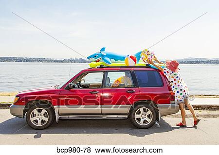 Woman takes beach toys and floaties off the roof of a car View Large Photo Image Stock Photo - Woman takes beach toys and floaties off the roof of a car. Fotosearch