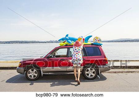 Woman takes beach toys and floaties off the roof of a car View Large Photo Image Stock Photo - Woman takes beach toys and floaties off the roof of a car. Fotosearch