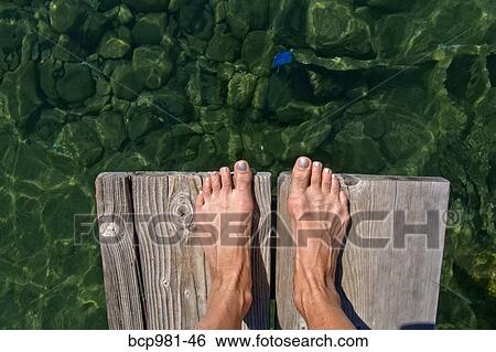 Stock Photograph - Woman's feet at the end of a dock over a lake. Fotosearch