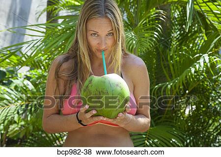Young woman in a bikini drinking from a coconut View Large Photo Image Stock Photo - Young woman in a bikini drinking from a coconut. Fotosearch