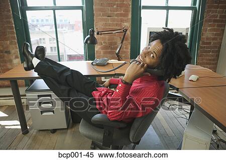 Stock Photography - A man talking on the phone with his feet on desk. . Fotosearch