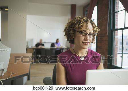 A woman sitting behind a laptop in a loft-style office. View Large Photo Image Stock Photo - A woman sitting behind a laptop in a loft-style office.. Fotosearch