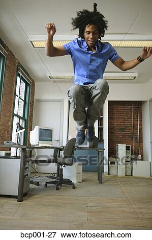 A young man leaping high in the air in a loft-style office. View Large Photo Image Stock Photo - A young man leaping high in the air in a loft-style office.. Fotosearch