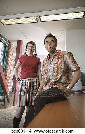 Two casually-dressed office workers at a desk. View Large Photo Image Picture - Two casually-dressed office workers at a desk.. Fotosearch