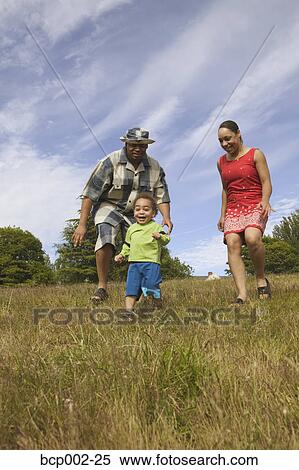 Stock Photography - A couple chasing their small son in a grassy field. . Fotosearch