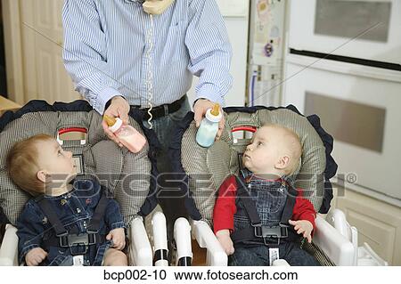 A father offering bottles to his twins. View Large Photo Image Stock Image - A father offering bottles to his twins.. Fotosearch