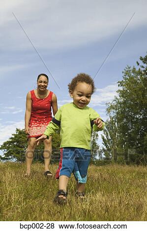 A mother watching her toddler walk in the grass. View Large Photo Image Stock Photo - A mother watching her toddler walk in the grass. . Fotosearch